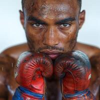 A determined African American male boxer with sweat on his face, holding worn boxing gloves close to his chin. photo