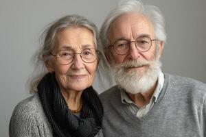 An elderly couple, smiling warmly, with gray hair and glasses, showcasing affection against a neutral background. photo