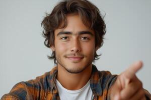 A young, smiling male with medium-length hair is pointing towards the viewer, exuding confidence and approachability. photo