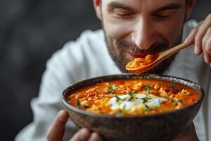 A smiling man enjoys a delicious bowl of creamy soup, highlighting vibrant colors and fresh herbs. photo