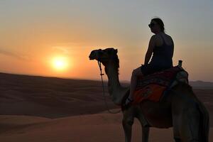 A woman riding a camel in the desert at sunset photo