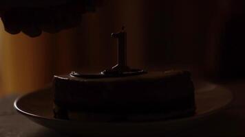 A cake with a minimum of details, decorated with one thin candle in the middle, the number 1. A hand brings a lighter to the candle and lights a fire video
