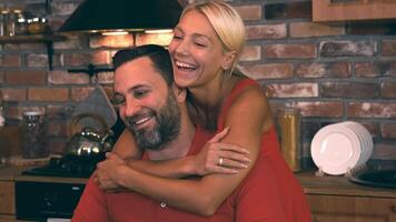 Beautiful blonde hugs her husband sitting in the kitchen at the dining table and they are smiling video