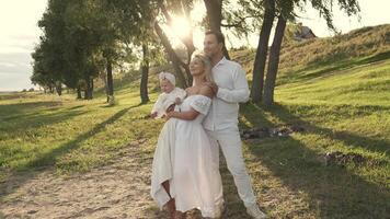 Happy family with little daughter standing on lawn during sunset. video