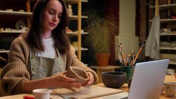 Pottery handmade art gallery potter artist designer sculptor student girl Caucasian woman decorator watch laptop call online tutorial teach creative craft workshop clay modeling pot handcraft video
