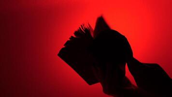 silhouette of an open book against a bright red background. Turning pages of a book. video