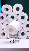 vertical Hand placing toilet paper roll in shopping cart with stacked rolls in background video