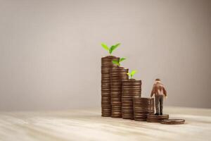 Elderly man doll walks up a pile of coins money with tree grows the amount of money. Concept of future growth in fixed deposit interest, dividends, stocks and retirement funds. photo