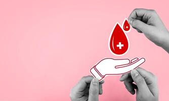 Top view of male hand holding a drop of blood with paper hands on pink background. With copy space. Concept of blood donation, health benefits for donors, blood banks, and World Blood Donor Day. photo