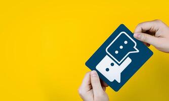 Hand holding a paper conversation speech bubble on yellow background. with copy space. Concept of communication, chat service, and business discussion photo
