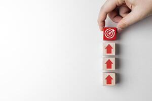 Hand places a red wooden block with a target and arrow pointing in the same direction. Concepts of planning, business investment goals, strategy and focus on achieving results. with copy space photo