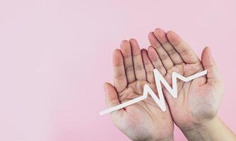 Paper ECG signal in hand on pink background. Concept of health care, atrial fibrillation, electrocardiogram, and heart disease. photo