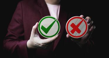 Businessman holds a circle of wood with green check mark and red cross icon. Right and wrong concept. checklists, approval lists, and test. photo