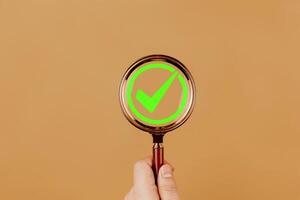 Magnifying glass with checkmark icon isolated on orange background. Concepts of checklists, approvals, completion processes, and quality assurance. photo