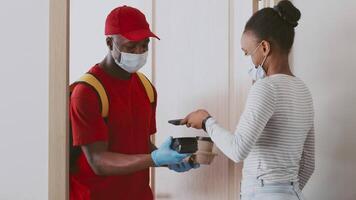 A man in a red cap hands over a delivery to a woman wearing a striped top at her apartment. Both are wearing masks and following safety protocols during home delivery. video
