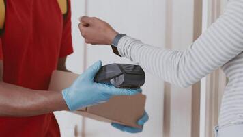 A man courier wearing gloves stands at the door of an apartment, scanning a package with a handheld device while a woman prepares to receive it. The setting reflects an urban residential area. video