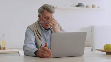 A senior man in his 60s focuses intently on his laptop while seated at a clean dining table. He enjoys his time at home, exploring technology as part of his retirement activities. video