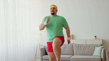 A young man engages in a workout routine at home, focused on improving his fitness and losing weight. He is wearing bright workout attire and appears motivated as he jogs in place. video