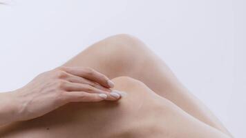 A young woman is applying moisturizer to her leg, focusing on skin care and self-pampering. The setting is isolated and calm, enhancing her relaxation and self-care routine. video