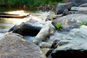 Shows a close-up of a riverbed with smooth rounded stones. Water is flowing gently over the rocks creating a blurred and ethereal effect. Glowing light in the river. photo