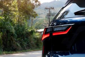 Rear side of dark with turn on brake light. side of car on aspahlt road with tree and grass in the countryside. photo
