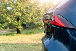 Partial rear view of a dark blue car. Possibly based on the tail light design. the car parking in garden with green grass with trees. photo