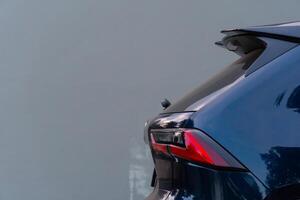 Partial rear view of a dark blue black SUV. Possibly based on the taillight design. The car is parked against a plain light-colored background. photo