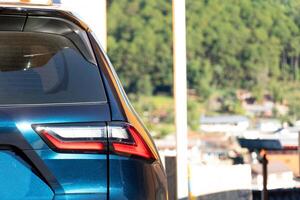 Close up of the rear of a blue car. Background shows greenery and buildings suggesting a mountainous or hilly area. Environment at day time. photo