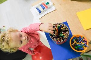 A toddler holding a pencil and a container of colored pencils photo