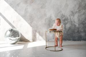 A baby is standing on a table with a cake photo