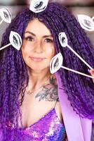 A woman with purple hair holding up some fake eyes photo
