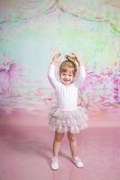 A little girl in a tutu standing in front of a pink background photo