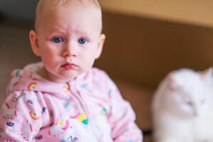 A baby sitting on the floor with a cat behind it photo