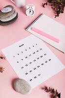 Calendar, alarm clock, notebook and pen on a pink background vertical view photo