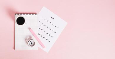 Calendar, alarm clock, notebook and pen on a pink background top view web banner photo