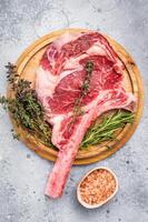Uncooked tomahawk steak, raw black angus beef rib eye with bone on wooden board. grey background. top view photo