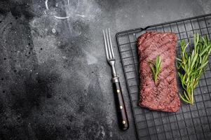 Grilled Flank steak, beef meat on rack with rosemary. black background. top view photo