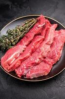 Raw sliced horse meat steaks presented with herbs and spices, inviting creativity in the kitchen for those seeking bold flavors and unique dining experiences. black background. top view photo