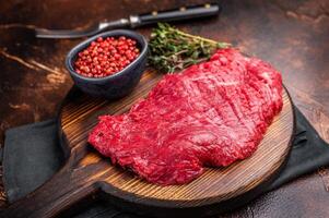 Flank or Flap steak, raw beef meat with thyme on wooden board. brown background. top view photo