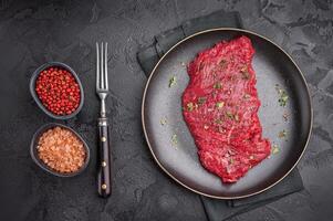 Marinated Flank or Flap steak, raw beef meat with thyme and spices on plate. black background. top view photo
