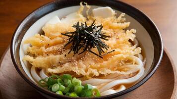 Delicious bowl of udon noodles topped with crispy tempura and garnished with green onions. photo