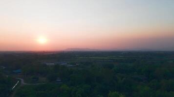 The golden sun slowly sets behind a silhouette of trees, casting long shadows and painting the sky with warm hues of orange and pink. A peaceful and calming moment captured in nature. video
