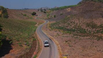 Experience a surreal drive on a white road through a dry, arid landscape, with sharp curves and towering trees lining the way. video