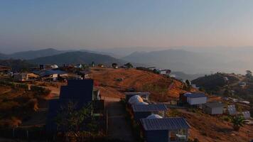 A breathtaking aerial view of a peaceful mountain village nestled among rolling hills. The vast sky stretches endlessly above, creating a serene and dreamlike landscape. video