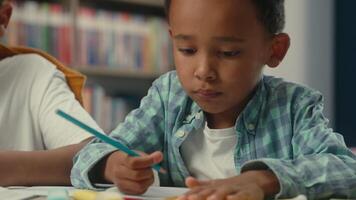 Little African American kid ethnic child boy son pupil toddler student schoolboy learner studying at desk writing drawing children primary elementary school education in classroom learn draw copybook video