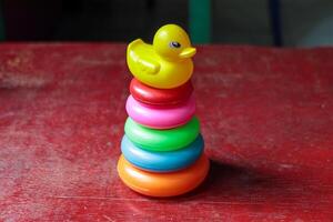 Colorful Stacking Toy with a Yellow Duck on a Red Wooden Surface photo
