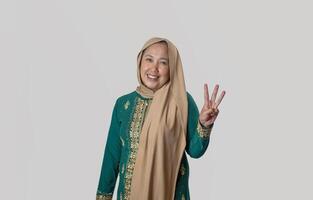 Smiling Woman in Traditional Green Attire Showing Three with Hand Gesture photo