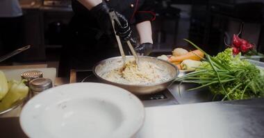 A woman in a chef's uniform puts ready-made pasta on a plate, a close-up of her hands, no face video
