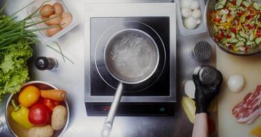 A woman in disposable black gloves adds salt to water boiling in a saucepan, close-up of her hands, top view video