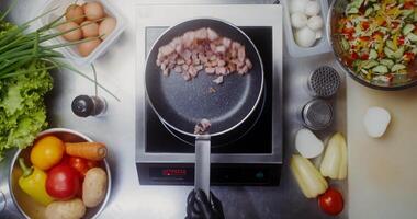A woman in disposable black gloves frying bacon in a frying pan tossing and stirring it, close-up of her hands, top view video
